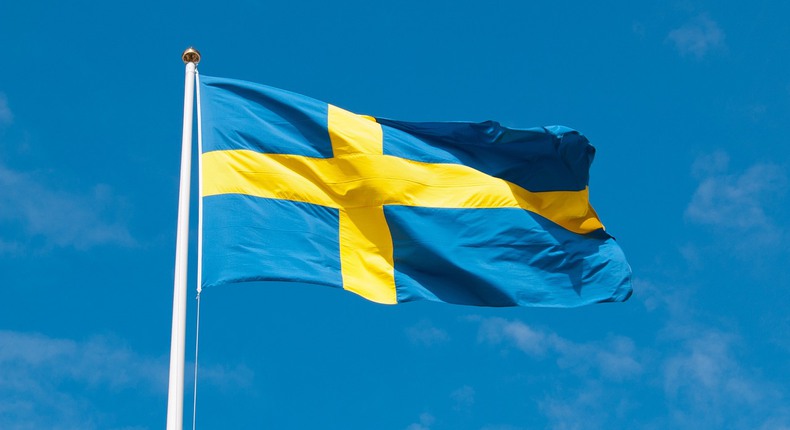 En svenska flagga, med ett gult liggande kors mot en blå bakgrund, hissad och fladdrandes mot en blå himmel.