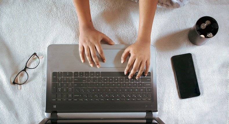 ett bord är två händer jobbar med laptopen medan mobil, glasögon och kaffemugg står bredvid